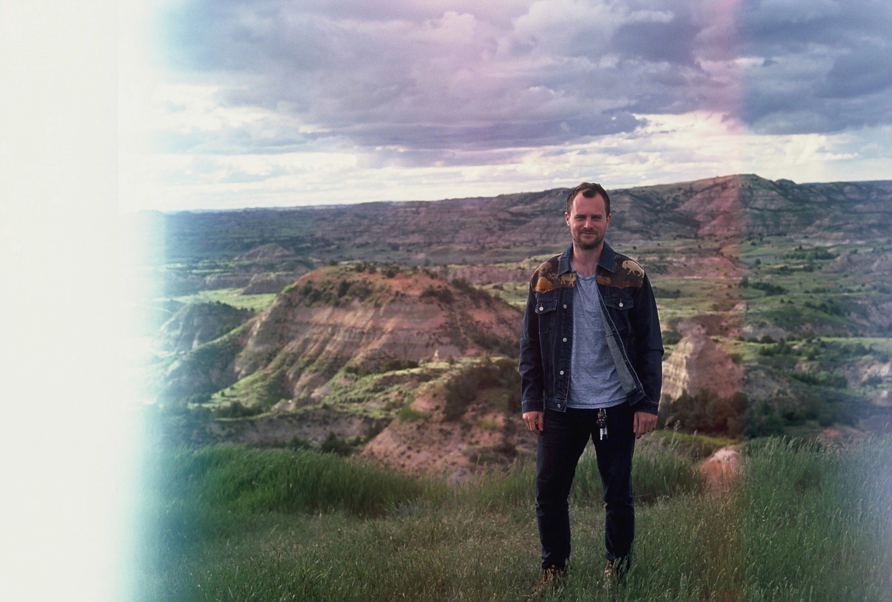 Wayne Wapeemukwa standing in the Badlands — eroded, rolling hills and open sky behind him.