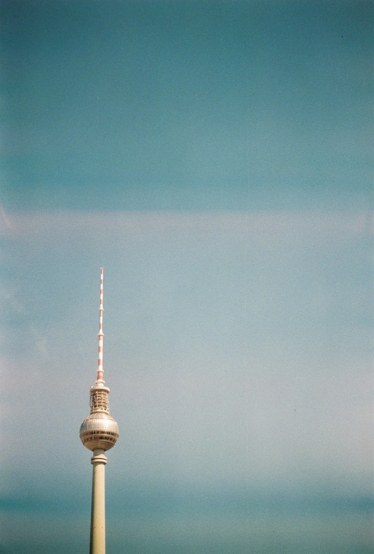A tall white and red telecommunications tower with a bulbous observation deck rises against a hazy blue sky.